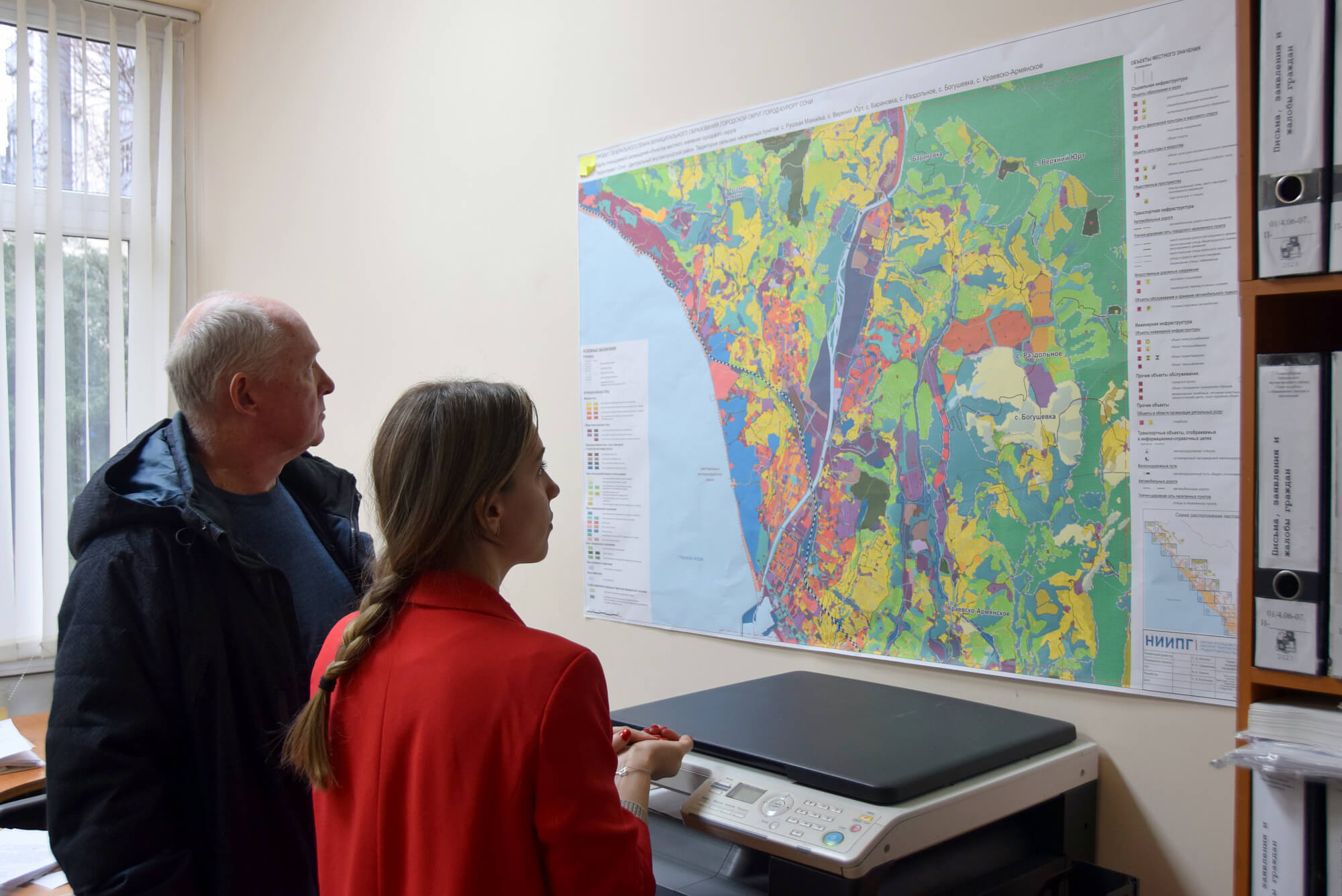 На фото мужчина и девушка рассматривают карту города Сочи со специальными зонами и слоями